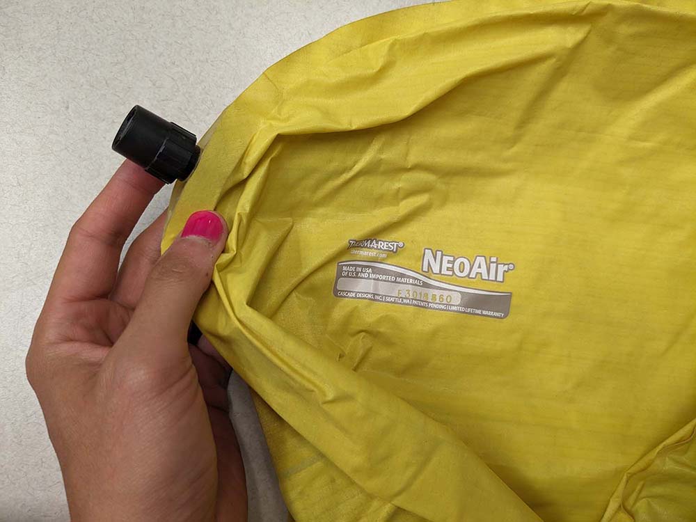 The top of a bright yellow Thermarest NeoAir Xlite with my hand holding the small valve.