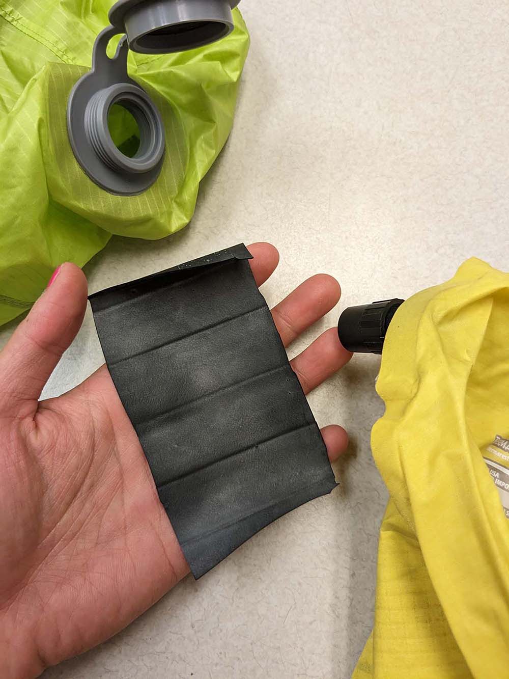 A rectangle of bike innertube rubber held in my hand next to the pump sack and sleeping pad.